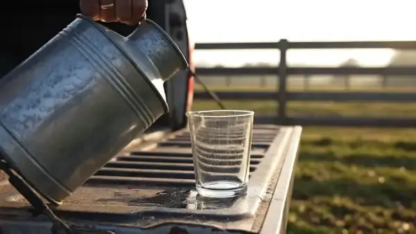Weathered hand pouring water from a steel jug into a glass on a pickup tailgate